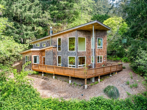 Modern retreat nestled among lush evergreens, featuring a spacious wraparound deck and floor-to-ceiling windows that invite natural light and forest views throughout.