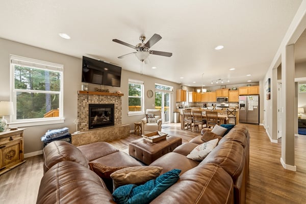 Sink into plush leather sofas in your open-concept living space, warmed by a cozy fireplace and ceiling fan. Large windows frame scenic views while the adjoining kitchen invites shared meals and laughter.
