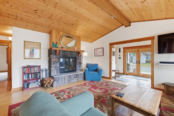 Cozy up by your stone fireplace while enjoying warm wood ceilings, comfortable seating, and peaceful garden views through French doors.