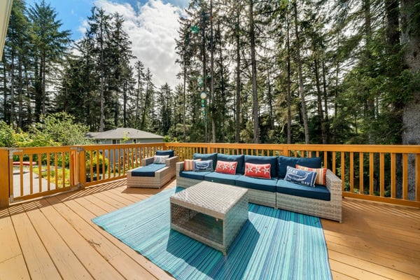 Expansive deck surrounded by towering evergreens offers a peaceful retreat with comfortable lounge seating overlooking the forested property setting.